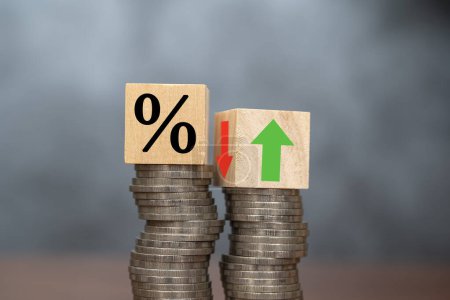 The concept of increasing or decreasing interest rates. Wooden cube with percentage icon Up and down symbols are placed on piles of coins on a dark background.