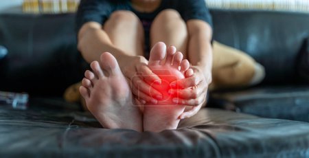 Photo for Close-up of young woman feeling pain in feet at home. Health care and medical concept. Young woman's pain is putting her hands on her feet, solving the problem of cramps caused by muscle spasm. - Royalty Free Image