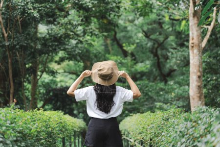 Foto de Vista posterior de la joven mujer sosteniendo ala sombrero de paja en la mano y disfrutando de la salida del sol en el lago del bosque en la mañana de verano con viajes de aventura - Imagen libre de derechos