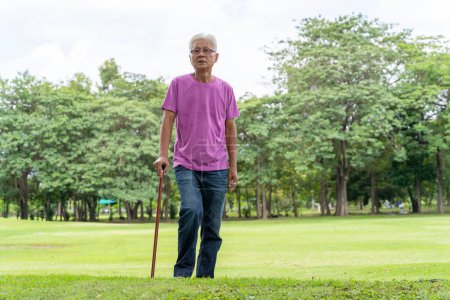 Vollständige Profilaufnahme eines älteren Mannes, der mit einem Stock in einem Park spaziert. Ein älterer Mann mit Gehstock steht in einem öffentlichen Park. Seniorenkonzept.