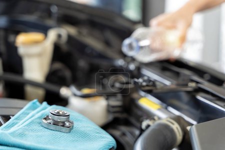 Photo for A woman takes matters into her own hands radiator refill. Mechanic performing car engine repair in an automotive service garage. A close-up of a hand adding water to the radiator cap of a car. - Royalty Free Image