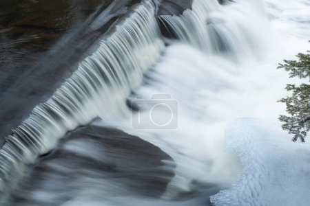 Winter landscape of a cascade at Bond Falls captured with motion blur and framed by ice, Michigan's Upper Peninsula, USA