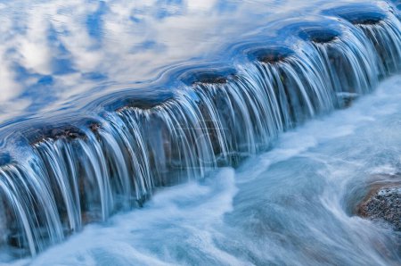 Téléchargez les photos : Paysage de la cascade du ruisseau Orangeville capturé avec flou au lever du soleil et illuminé par le ciel bleu et les nuages au-dessus, Michigan, États-Unis - en image libre de droit