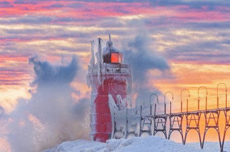Téléchargez les photos : Paysage hivernal au coucher du soleil du phare glacé de South Haven, jetée et passerelle avec vagues éclaboussantes, lac Michigan, Michigan, États-Unis - en image libre de droit