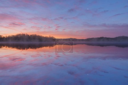 Foto de Paisaje al amanecer de la costa del lago Whitford con reflejos espejados en aguas tranquilas y luna creciente, Fort Custer State Park, Michigan, EE.UU. - Imagen libre de derechos