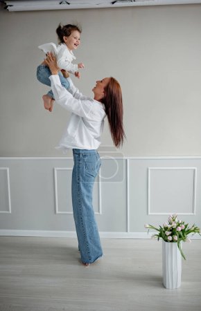 Photo for Happy young mom playing with her child girl lifting her up. Mother and daughter having fun together - Royalty Free Image