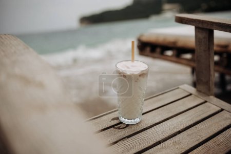 Summer holiday concept. Vintage colours. White coconut ice cream cocktail on wooden chair by the sea.