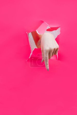 Eine Frau zeigt mit dem Finger durch eine zerrissene rosafarbene Papierwand. Handbewegungen der Richtung
