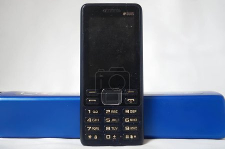 Téléchargez les photos : Un téléphone noir à bascule repose sur un objet bleu. Photo de haute qualité - en image libre de droit