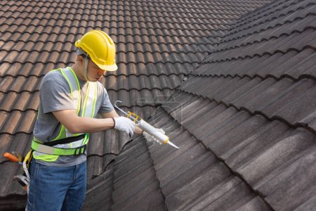 Foto de Hombre trabajador que utiliza adhesivo sellador de silicona para fijar la grieta del techo de baldosas viejas. - Imagen libre de derechos