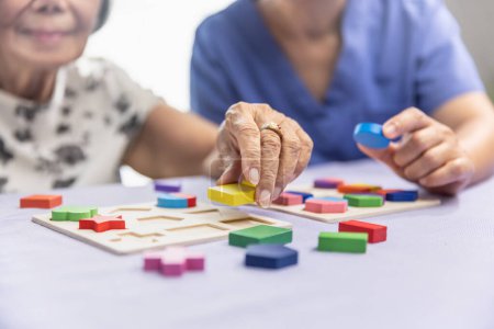 Téléchargez les photos : Aide-soignant et femme âgée jouant jeu de puzzles en bois pour la prévention de la démence - en image libre de droit