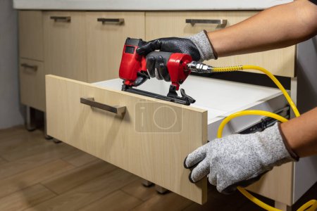 Téléchargez les photos : Réparation des travailleurs tiroir en bois de l'armoire avec pistolet à ongles pneumatique. - en image libre de droit