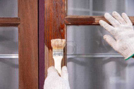 Téléchargez les photos : Travailleur utiliser brosse appliquer le préservateur de bois après ponçage de l'ancienne surface de la fenêtre en bois - en image libre de droit