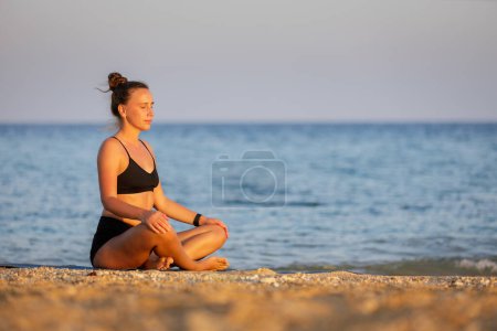 Matin méditation en plein air à la plage. Femme de forme physique respirant et méditant près de la mer au coucher du soleil. Image avec espace de copie