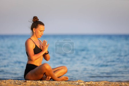 Morning outdoor meditation at the beach. Fitness woman breathing and meditating near the sea at sunset. Image with copyspace