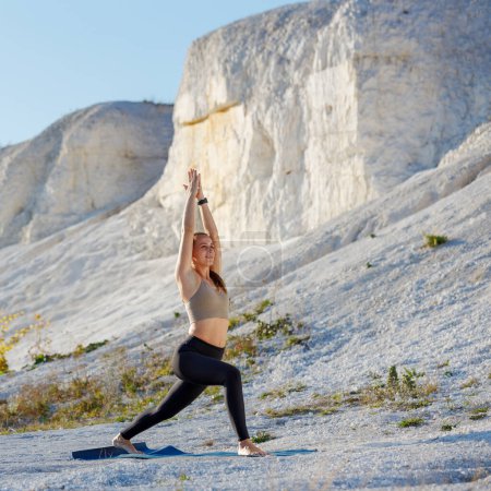 Yoga al aire libre practicando al amanecer. Mujer de fitness haciendo pose de alta embestida cerca de las rocas blancas