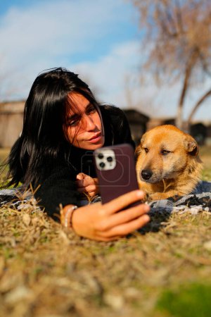 Photo for A beautiful brunette in a black sweater, lies on the grass with a homeless dog, the girl hugs the dog, takes pictures with him and takes care of him, a beautiful red dog - Royalty Free Image