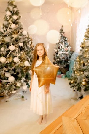 Foto de Hermosa niña se ríe y se para cerca de los árboles de Navidad con un globo de estrella. concepto de la infancia feliz, pidiendo un deseo para el año nuevo y cumpleaños. - Imagen libre de derechos