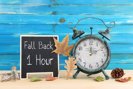 Photo for Image of autumn Time Change. Fall back concept. Dry leaves and vintage alarm Clock on rustic wooden table - Royalty Free Image