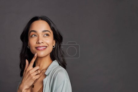 Photo for Portrait of pensive young mixed race woman with hand on chin looking away isolated on gray background. Multiethnic beautiful girl in casual clothing isolated against grey wall daydreaming with copy space. Close up face of happy mexican woman thinking - Royalty Free Image