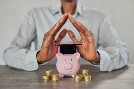 Photo for Close up of businesswoman hands showing sign of protection for graduation savings on piggy bank. African woman saving money for children education. Student loan, education savings and scholarship concept. - Royalty Free Image