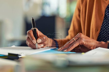 Photo for Close up of african american business woman hands writing on report while working in office. Successful black woman signing documents at home using a pen. Mid adult freelancer signing contract document on table. - Royalty Free Image