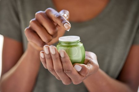 Photo for Close up of african american woman hands holding a green cream jar in palm. Woman hand holding anti-aging lotion in hand. Black woman applying moisturizer. - Royalty Free Image