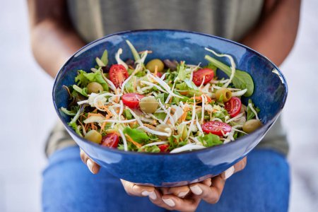 Photo for Hands of african american woman holding bowl with fresh salad of cabbage, tomato and green leaves. High angle view of healthy woman holding bowl of delicious and fresh salad. Vegan, dieting food concept. - Royalty Free Image