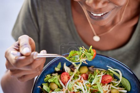 Photo for Close up of happy black woman eating healthy salad with green fresh ingredients. Smiling vegetarian woman holds bowl of fresh salad while eating tomatoes and carrot with fork. Detail of beautiful african american lady eating vegan food at home during - Royalty Free Image