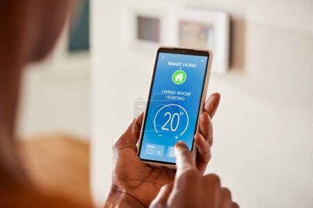 Photo for Close up of black hand setting temperature of air conditioner using mobile phone at home. African american woman use smart home app on phone in living room to adjust temperature and ventilation. Woman holding a smartphone adjusting heating with home - Royalty Free Image