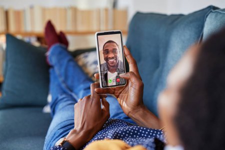 Photo for African american woman enjoying video call using smartphone with boyfriend while relaxing on couch. Close up of african man on mobile phone having a conversation with girlfriend through videocall. Closeup of black wife holding phone and talking to he - Royalty Free Image