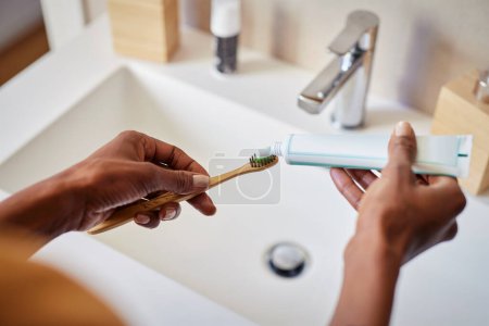 Photo for Black woman hand squeezing whitening paste on wooden toothbrush, taking care about mouth hygiene. Close up of female hands applying toothpaste on ecological bamboo tooth brush, plastic free concept. Oral hygiene and environmental responsibility conce - Royalty Free Image