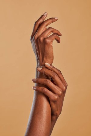 Foto de Mujer afroamericana manos aplicando crema hidratante. Mujer negra gestos de belleza con las manos aisladas sobre fondo marrón. Las manos elegantes femeninas se tocan con un movimiento de ligereza. - Imagen libre de derechos