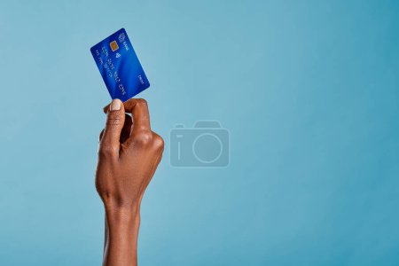 Photo for Close up of african woman hand holding bank credit card to make a payment with copy space. Black woman hand holding credit card for financial transaction or contact less payment isolated on blue background. African american woman showing debit card. - Royalty Free Image