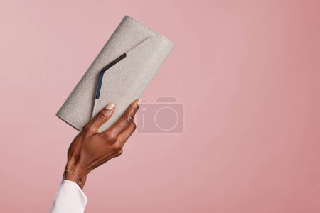 Photo for Female black hand holding elegant silver bag against red background. Hands of african american glamour woman holding purse isolated isolated with copy space. Fashion girl showing her new stylish clutch purse purchased during the sales. - Royalty Free Image