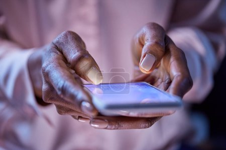 Photo for Close up of woman hands using mobile phone in dark. Hands of african american woman using smartphone to message. Black girl holding and typing on smart phone. - Royalty Free Image