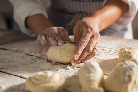 Photo for Professional baker hands kneading dough while preparing bread loaves in the early morning. Woman hands preparing bread loaf while cooking homemade in kitchen. Mixing and kneading wheat flour in the bakery. - Royalty Free Image