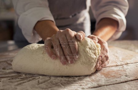Téléchargez les photos : Gros plan des mains du boulanger pétrissant la pâte au petit matin. Pâte naturelle et biologique à base de farine et levure sur table en bois. Les mains de la femme pétrissent la pâte pour faire du pain frais à la boulangerie. - en image libre de droit