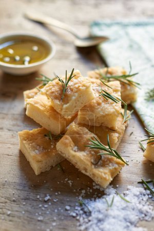 Photo for Tasty and healthy rosemary focaccia bread composition with salt, oil and leaves. Typical salty flat bread with rosemary made in Liguria, Italy. Italian focaccia bread with herb in slices. - Royalty Free Image