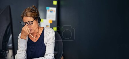 Photo for Tired businesswoman wearing headphone suffering from migraine after heavy and stressful day in office. Hispanic business woman feeling unhappy working from home: overworked and burnout concept. Upset lady wearing eyeglasses with headset and suffering - Royalty Free Image