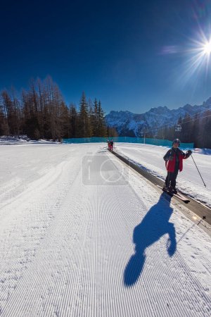 Téléchargez les photos : Falcade, Italie - 18 février 2023 : jeune homme sur un tapis roulant de téléski, communément appelé tapis magique. Ses skis reposent sur la surface mobile, prêts à être transportés - en image libre de droit