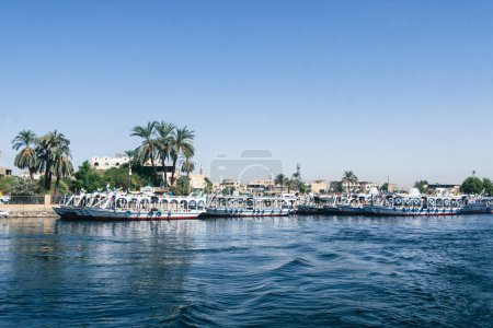 Téléchargez les photos : Plongez dans la beauté de Louxor en naviguant le long des eaux tranquilles du Nil. Cette photo à couper le souffle capture le port animé de Louxor, encadré par la silhouette de la tradition - en image libre de droit