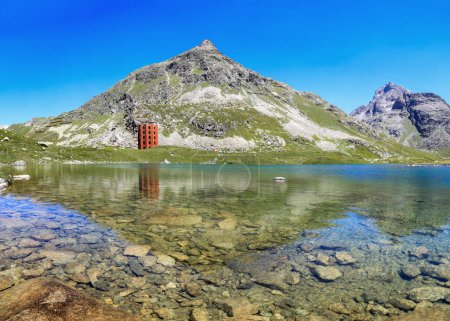 Photo for Grisons, Switzerland - June 25. 2023:The red Julier Theater Tower on the Julier Pass (2284 m above sea level) with reflection on Lake Culuonnas and Chueren Nair Peak at background - Royalty Free Image