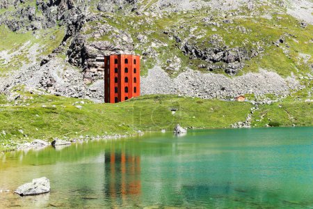 Photo for Grisons, Switzerland - June 25. 2023:The red Julier Theater Tower on the Julier Pass (2284 m above sea level) with reflection on Lake Culuonnas. - Royalty Free Image