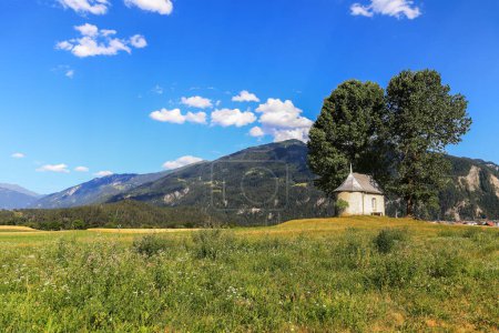 Téléchargez les photos : La chapelle Sogn Mang à Bonaduz, les Grisons en plein champ avec de grands peupliers luxuriants en été - en image libre de droit