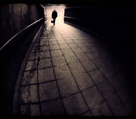 Photo for Silhouette of man entering a dark tunnel in bronze monochrome - Royalty Free Image