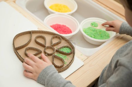 Photo for Easter concept. Boy plays with colored rice. Implement for children to develop fine motoric skills through play. DIY toy to learn hand - eye coordination. Montessori type pre school activities at home - Royalty Free Image
