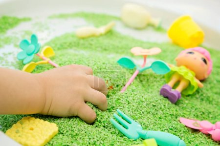 Junge spielt mit grüner Farbe Reis. Rollenspiel - Blumen pflanzen. Spielerisch sollen die Kinder ihre Feinmotorik entwickeln. DIY-Spielzeug zum Erlernen der Hand-Auge-Koordination.