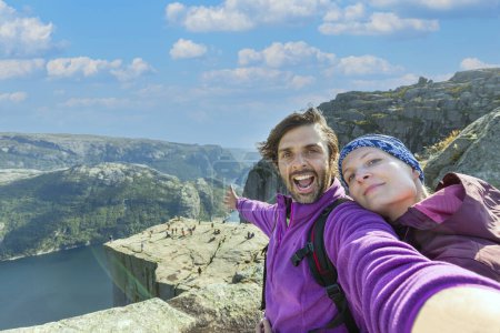 Photo for Couple taking a selfie on a rock and admiring a view on Preikestolen. Aerial shot, upper perspective on the couple. Endless view of the fjord. - Royalty Free Image