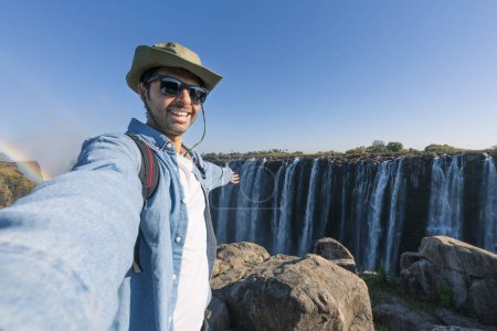 Foto de Un turista se toma un selfie en las cataratas Victoria en el río Zambezi, ubicado en la frontera entre Zambia y Zimbabwe, la cascada más grande del mundo. - Imagen libre de derechos